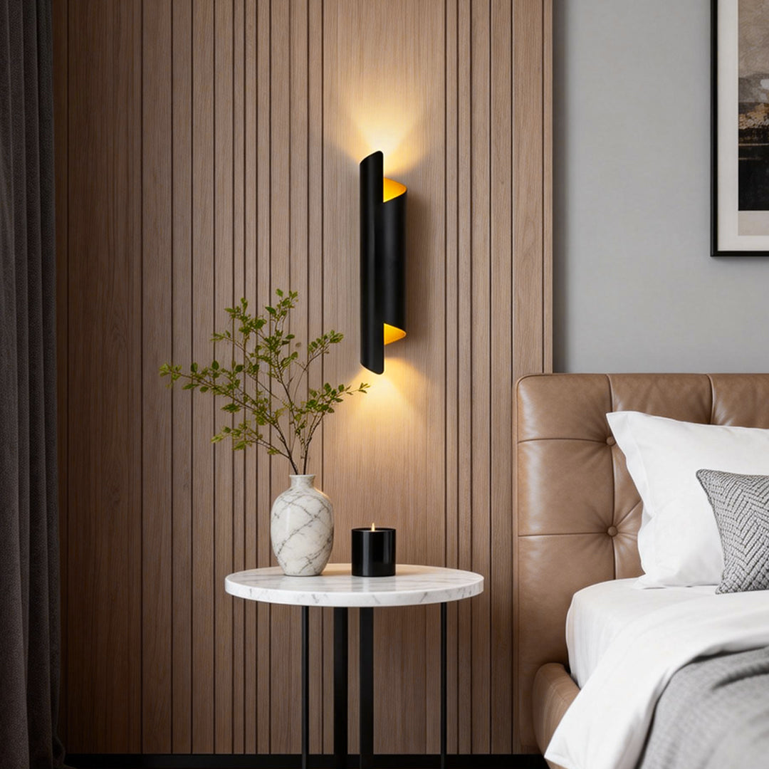 Modern scroll wall sconce in black and gold, mounted beside a bed for stylish and functional bedroom lighting.