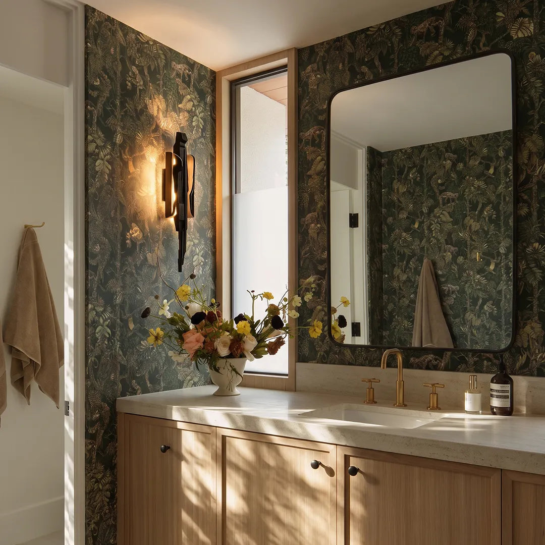 Modern sculptural wall sconce mounted beside a bathroom mirror with dark patterned walls and a wood vanity.