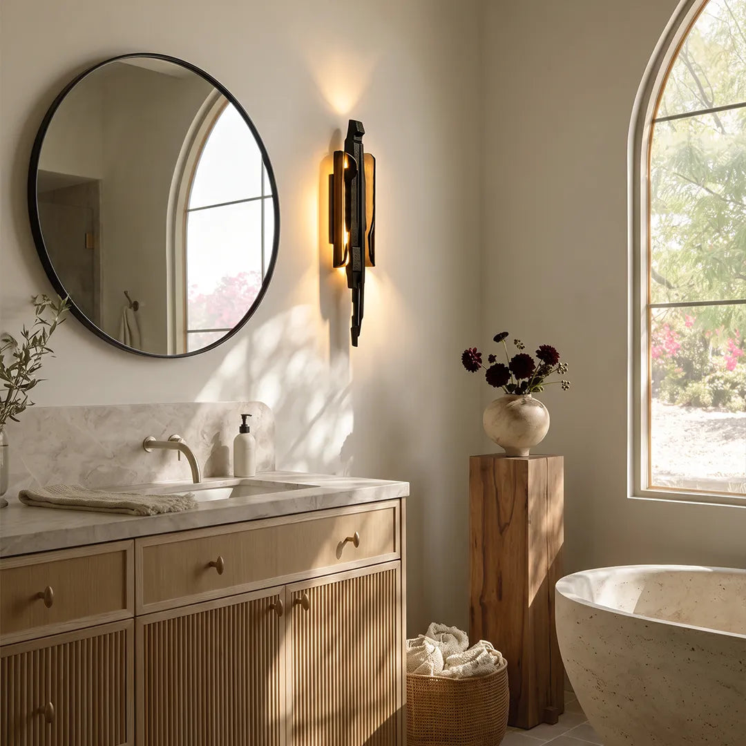 Modern sculptural wall sconce accenting a bathroom vanity and freestanding tub beside an arched window.