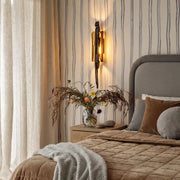 Modern sculptural wall sconce installed beside a bed with soft neutral bedding and striped wall paneling.