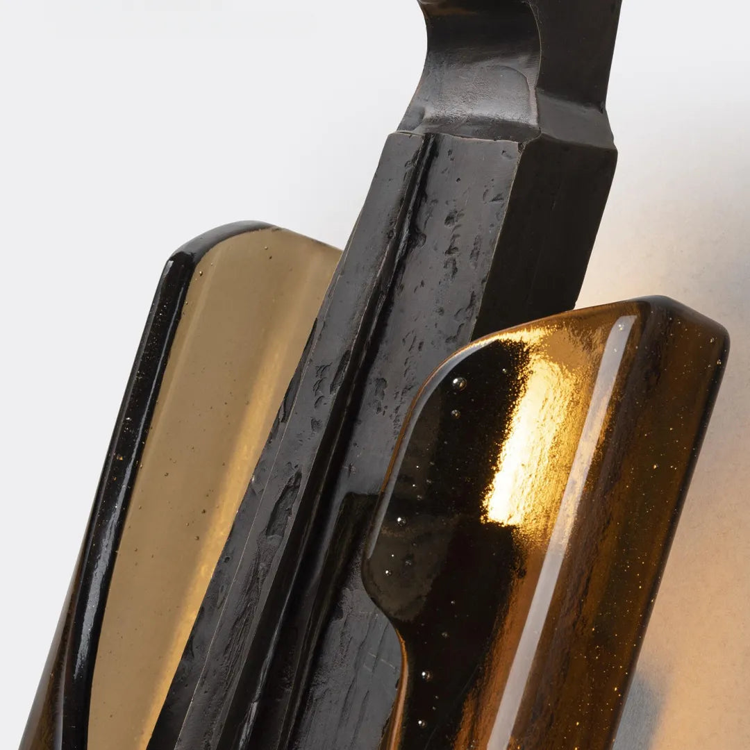 Modern sculptural wall sconce close-up showing layered black metal and amber glass details.
