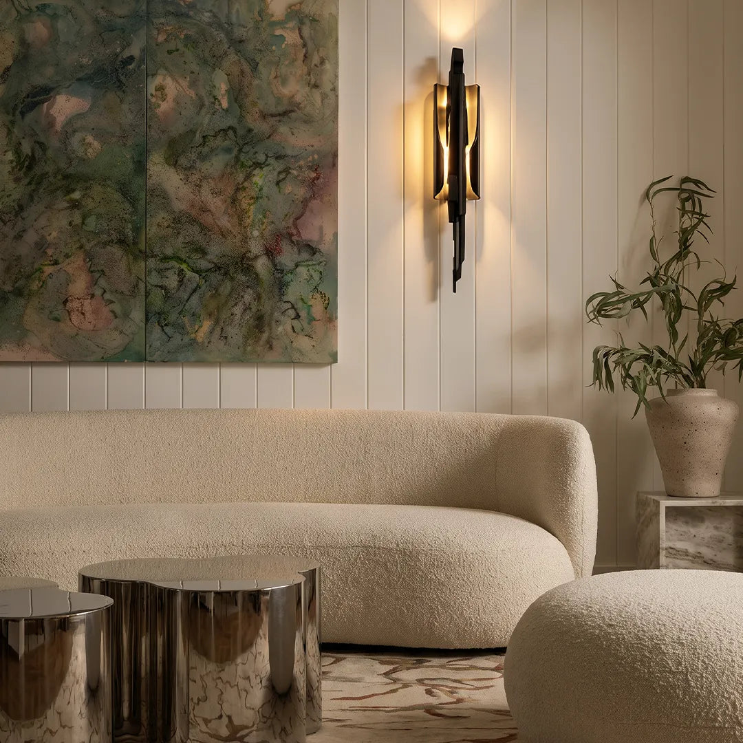 Modern sculptural wall sconce adding warm ambient light above a curved sofa in a contemporary living room.