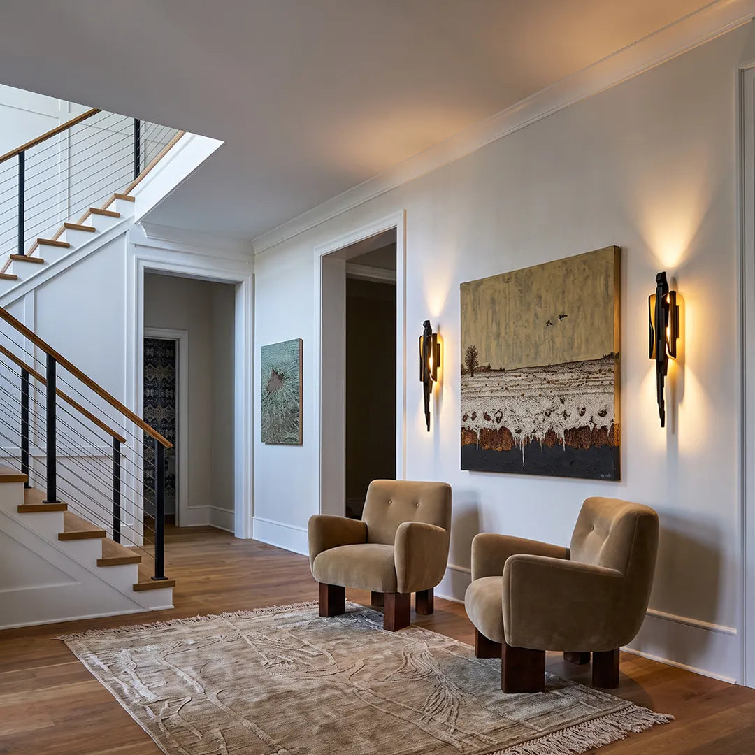 Modern sculptural wall sconce lighting a hallway seating area with armchairs and abstract wall art.