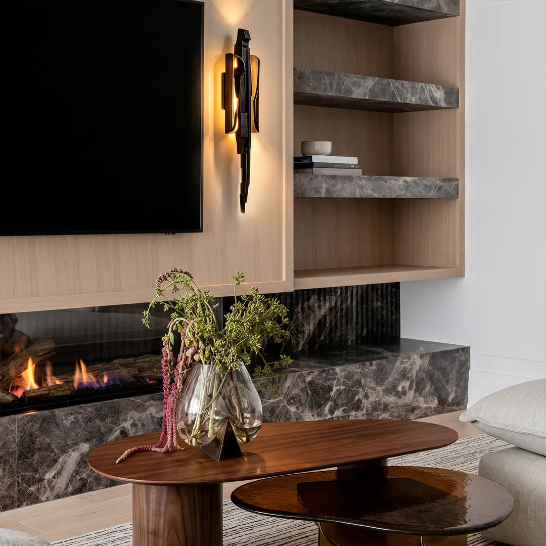 Modern sculptural wall sconce mounted beside a TV wall and fireplace with wood shelving and marble accents.