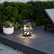 A modern short black lighted outdoor planter with cutout designs glowing on a grey composite deck.