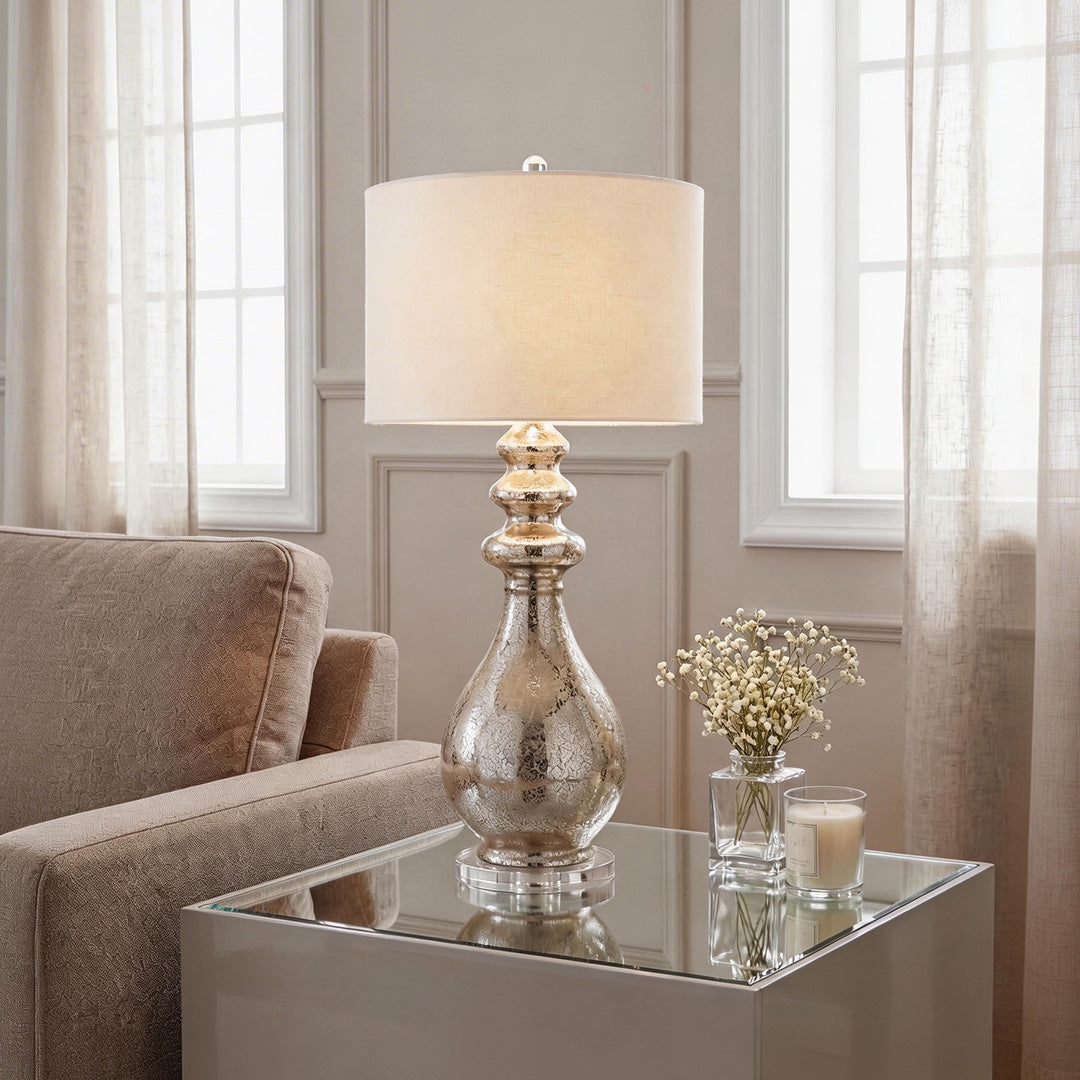 Elegant modern silver mercury glass table lamp with a cream drum shade on a mirrored side table.