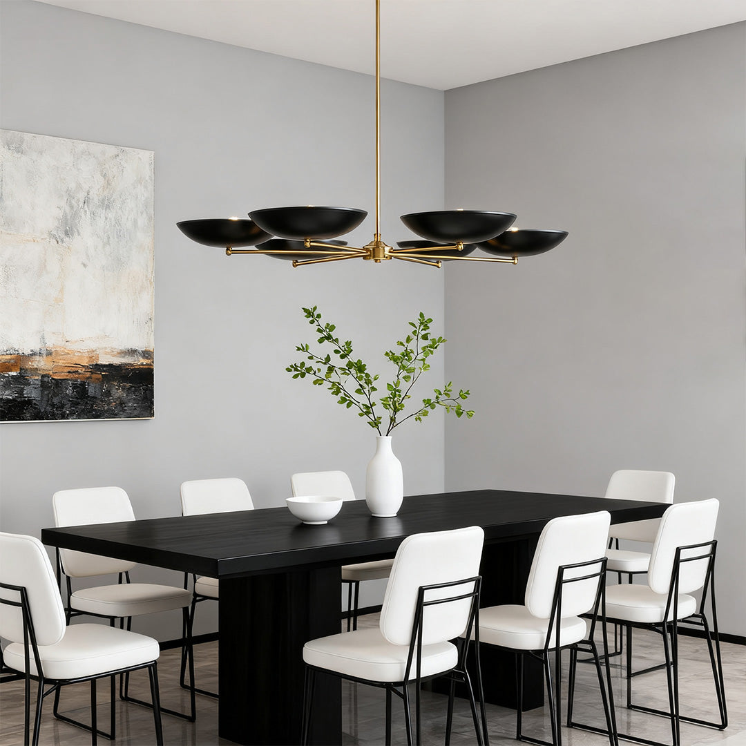 Modern six-light black and gold chandeliers with disc shades, centered over a long black dining table in a minimalist setting.