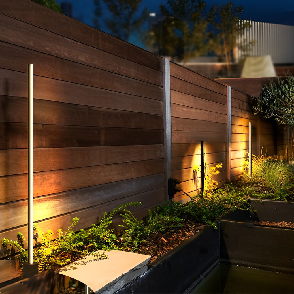 Modern slim bollard style contemporary outdoor floor lamps used beside a wooden outdoor wall at night.