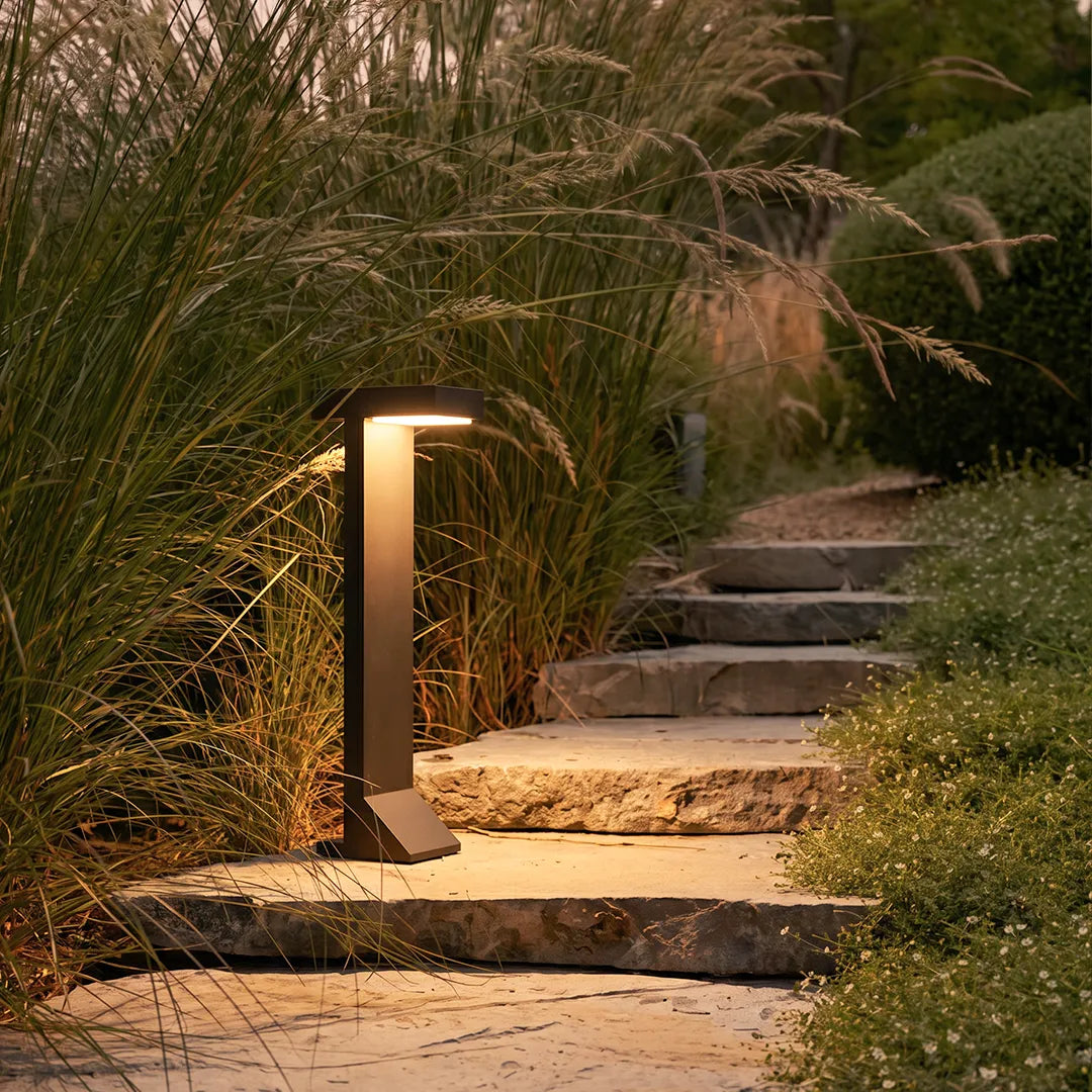 Modern solar bollard light illuminating stone garden steps and ornamental grasses