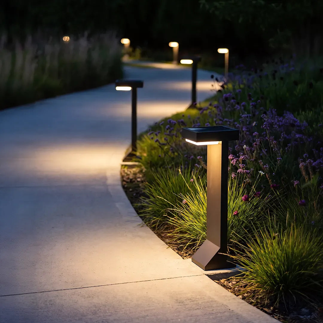 Modern solar bollard lights with warm glow along curved garden walkway at night