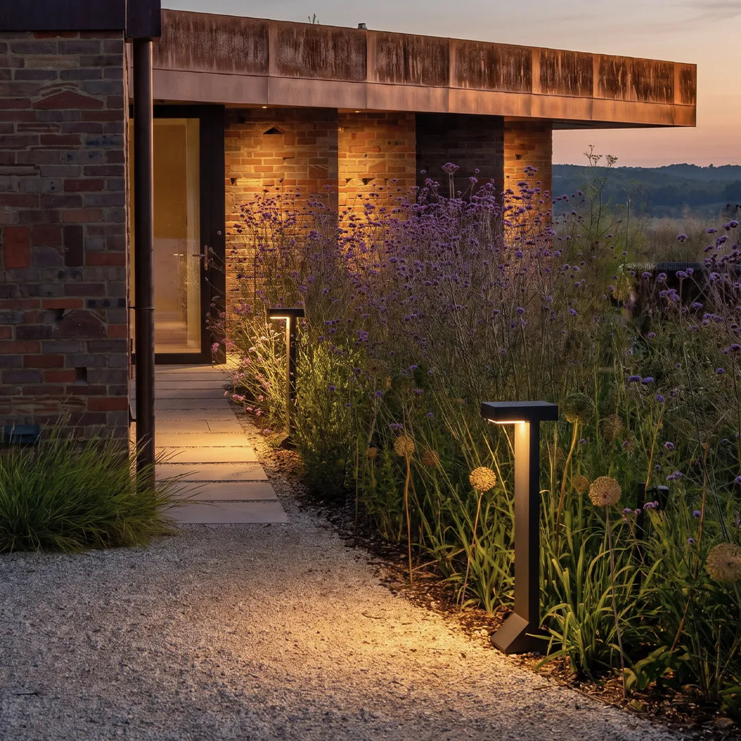 Modern solar bollard lights with warm glow along flower garden walkway