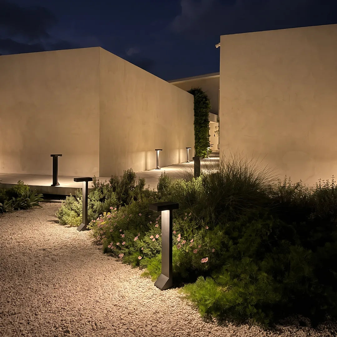Modern solar bollard lights illuminating gravel garden path beside concrete walls