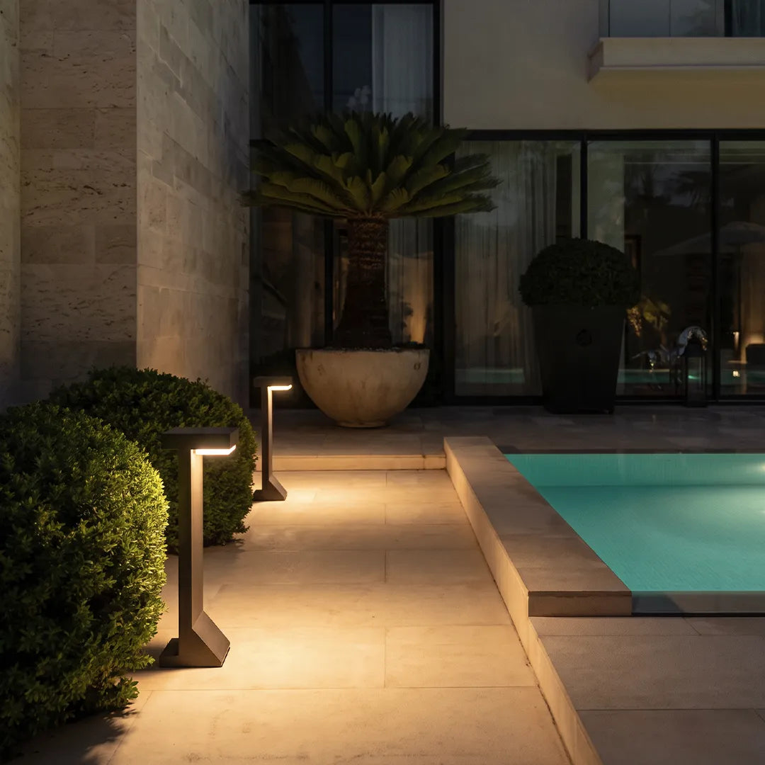Modern solar bollard lights illuminating poolside patio and garden shrubs