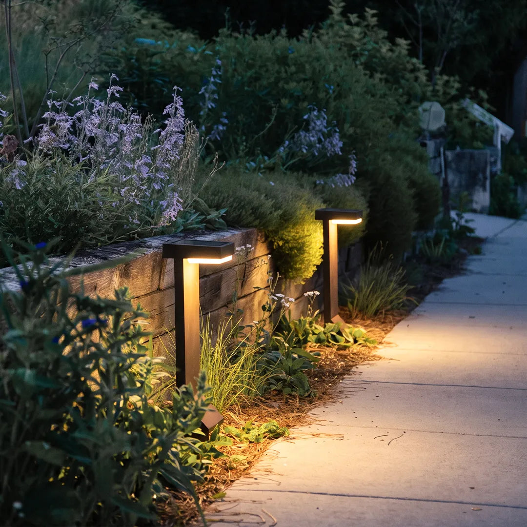 Modern solar bollard lights with warm glow along stone garden pathway
