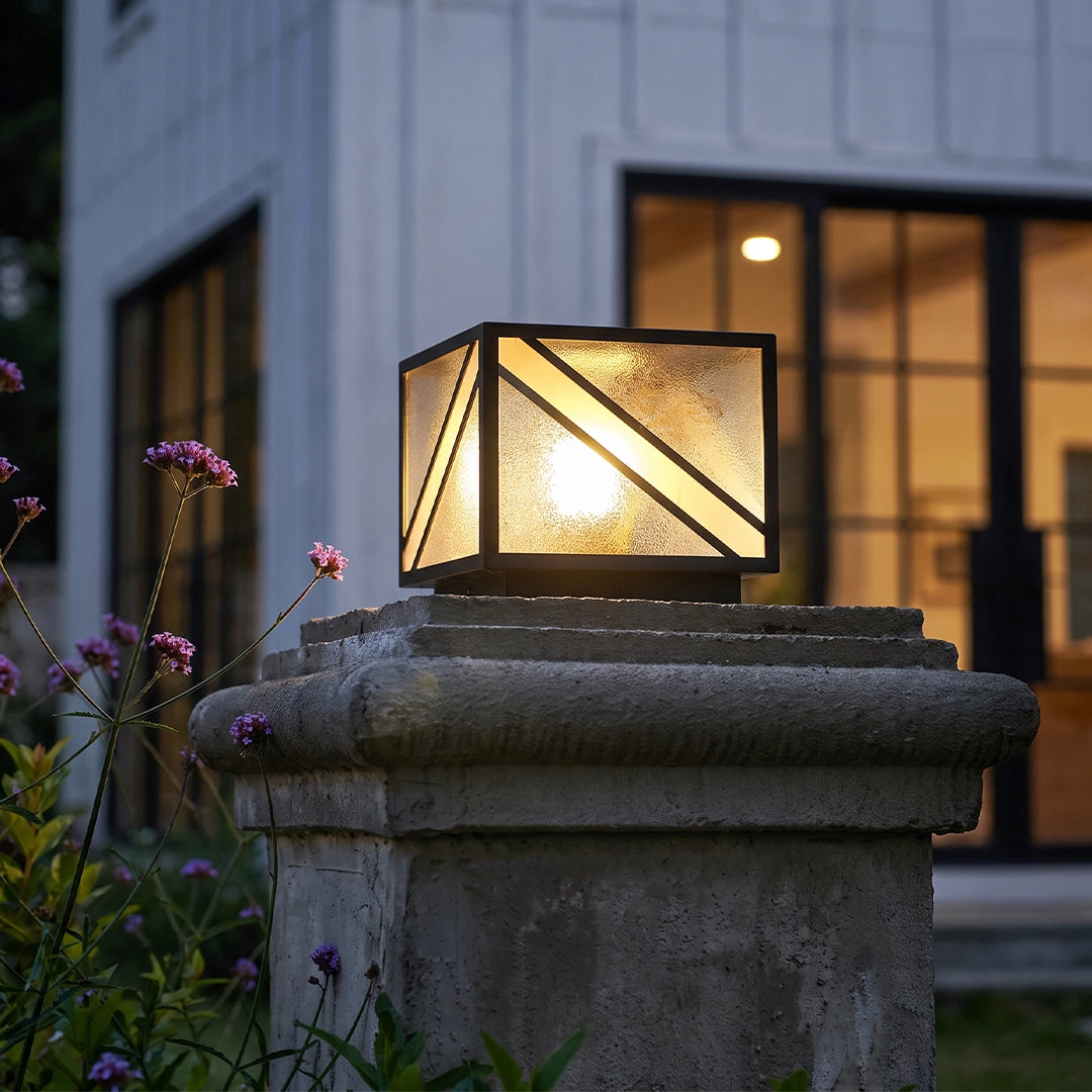 Modern solar pillar light with warm glow on stone column beside front yard