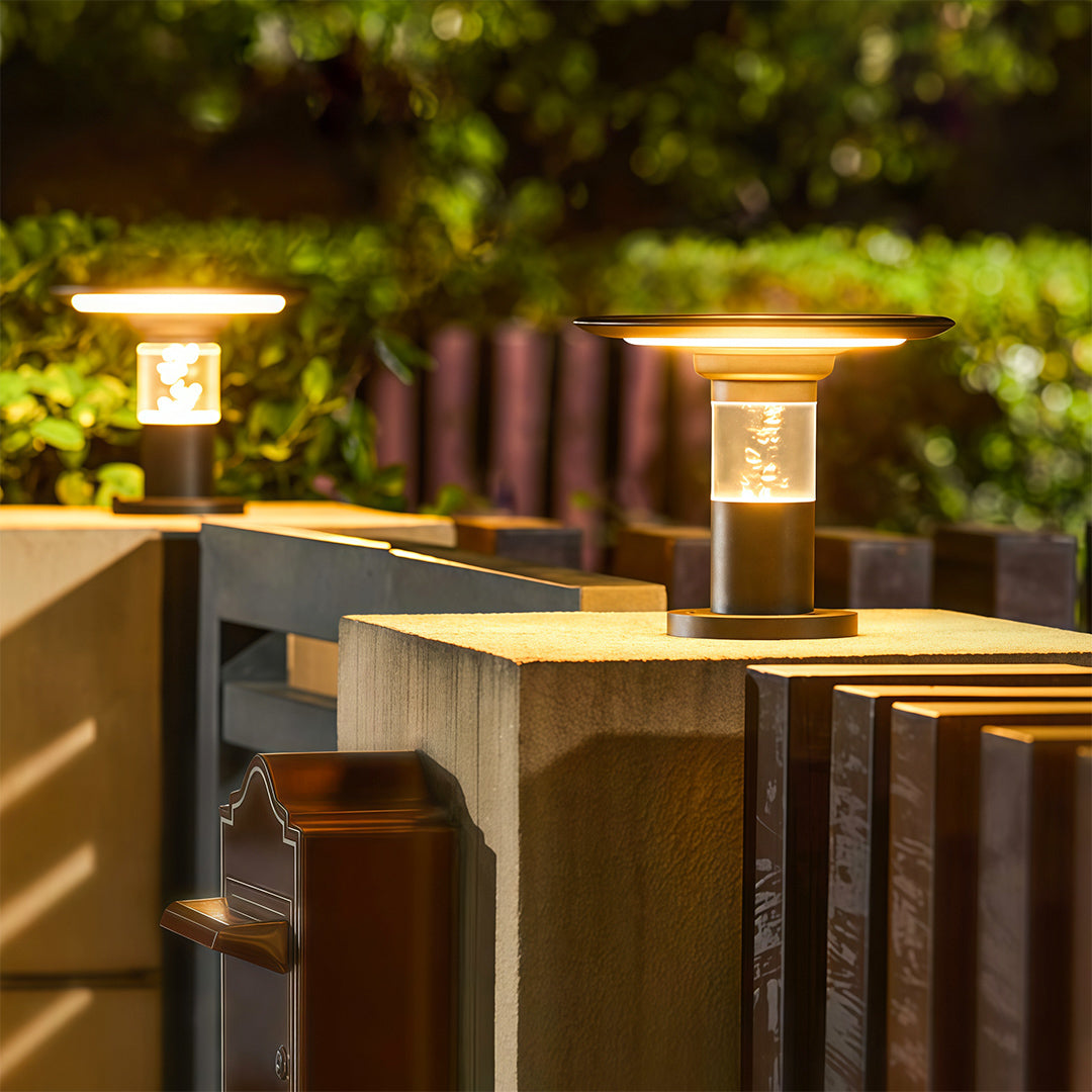 Modern solar post cap light fixtures with bubble glass, shown glowing warmly on a concrete and wood fence.