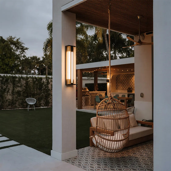 Modern solar wall sconce with warm glow beside covered patio and outdoor lounge