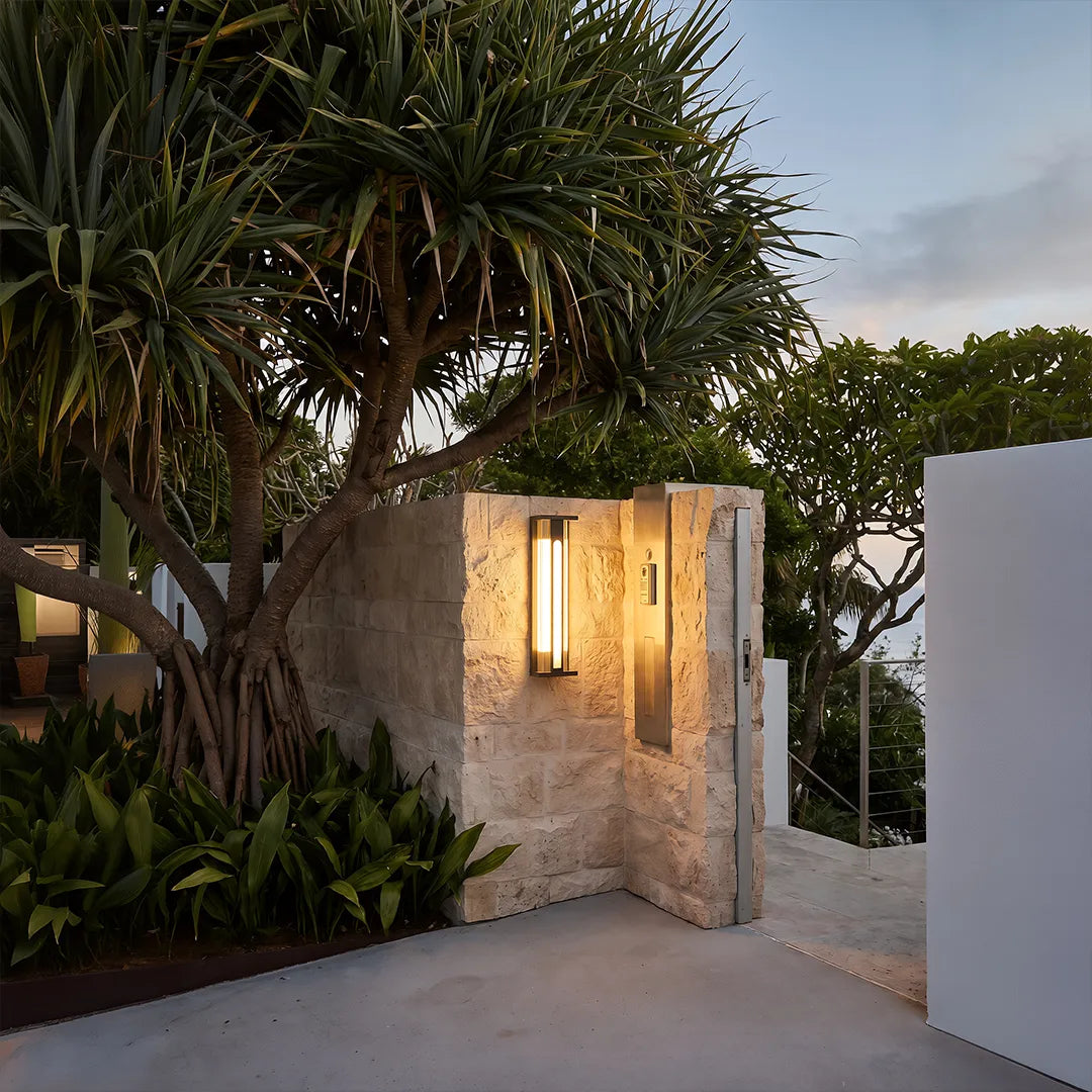 Modern solar wall sconce with warm glow beside stone garden entrance
