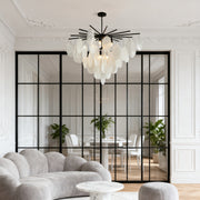 Modern starburst mother of pearl chandelier with black spokes, defining an open-plan living and dining area with glass partition walls.
