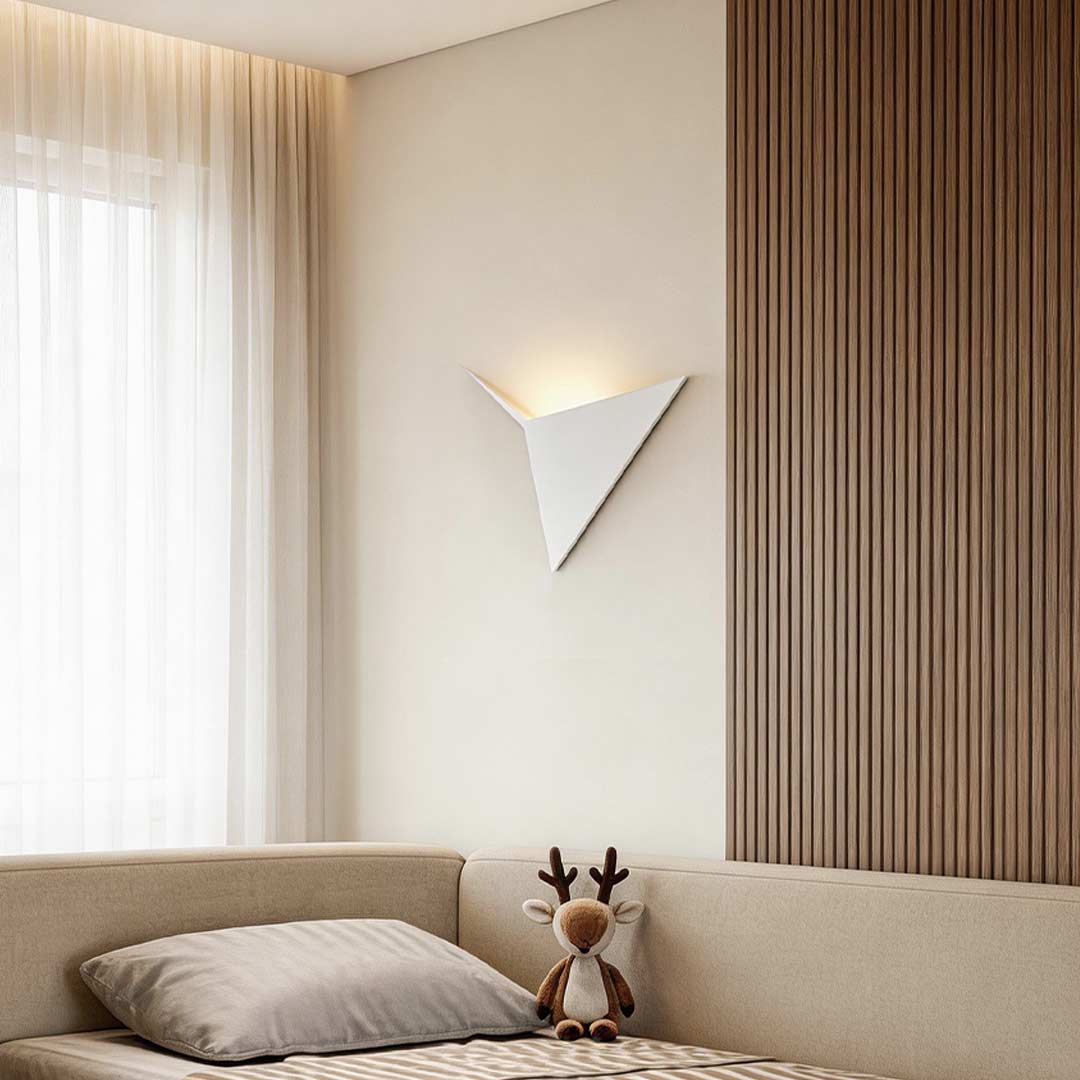 Modern triangle wall sconce illuminating a cozy bedroom corner with warm directional glow.