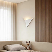 Modern triangle wall sconce illuminating a cozy bedroom corner with warm directional glow.