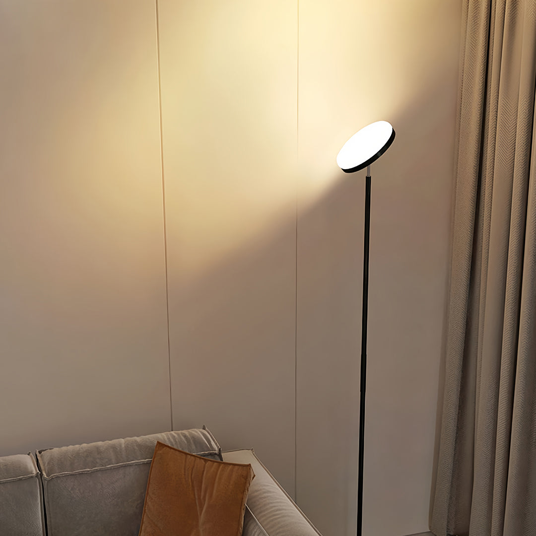 Modern uplight floor lamp with sleek black pole and circular LED top providing ambient ceiling illumination