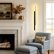 Modern vertical wall light mounted beside a fireplace and blue accent chair in a cozy living room.