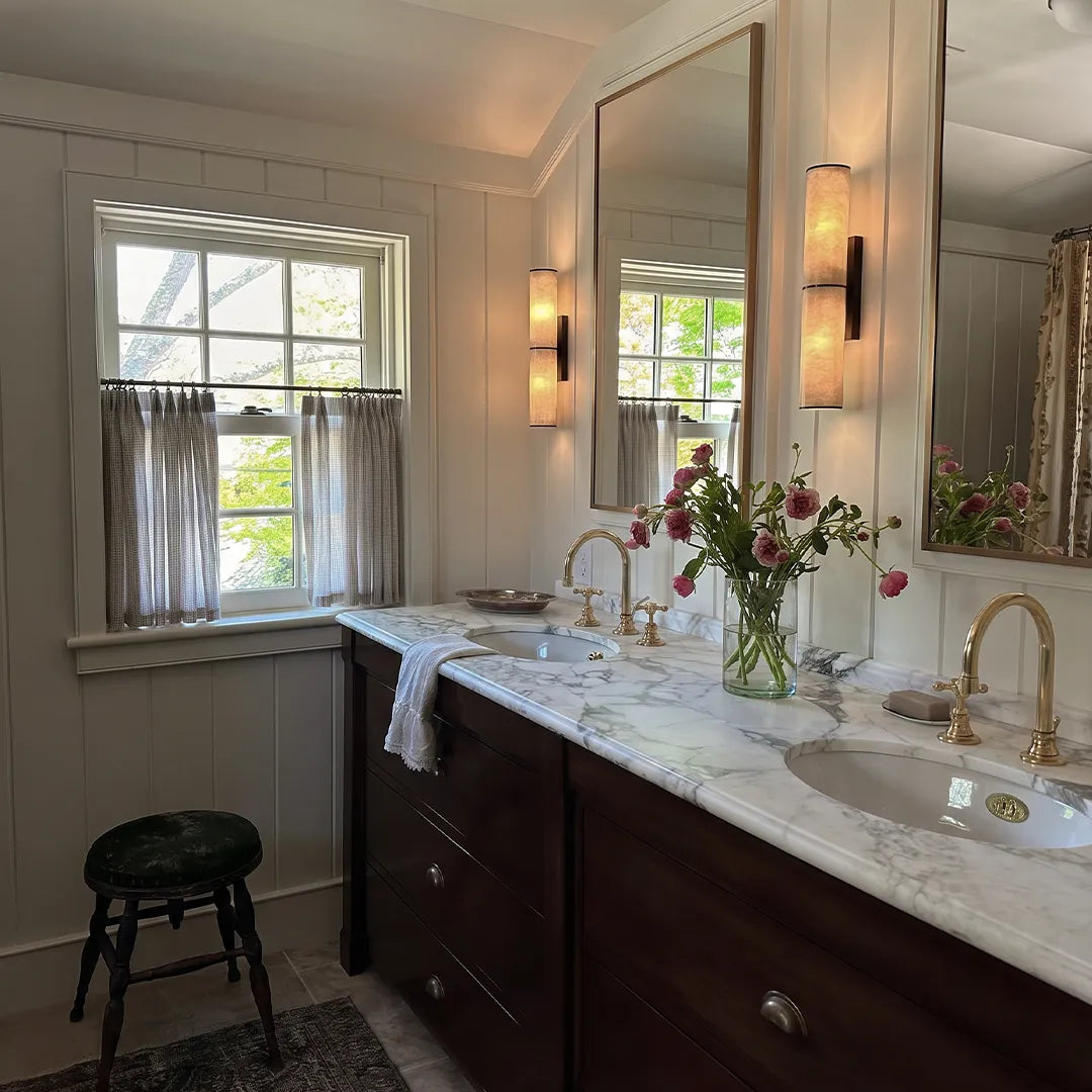 Modern vertical wall sconce installed beside a bathroom mirror above a double vanity.