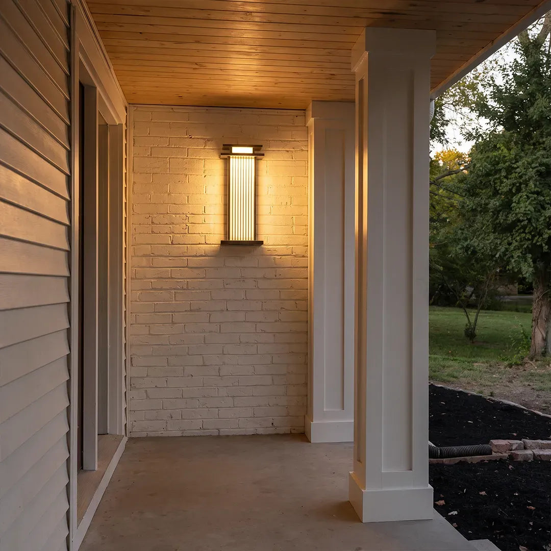 Modern vertical wall sconce illuminating a covered porch with a warm ambient light.