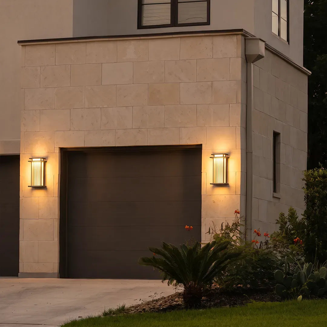 Modern vertical wall sconces flanking a garage door on a beige stone exterior at dusk.