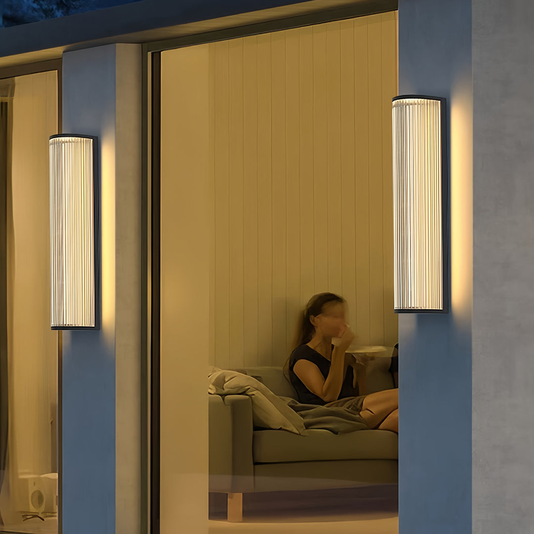 Modern vertical wall sconce lighting illuminating an outdoor patio and entryway of a contemporary home at dusk.