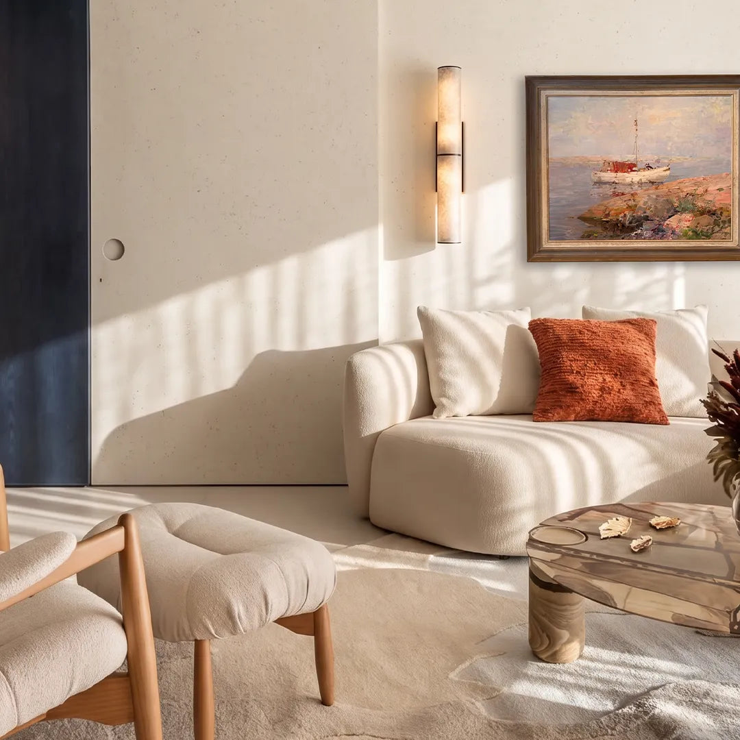 Modern vertical wall sconce mounted beside a sofa in a sunlit neutral-toned sitting area.