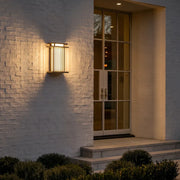 Modern vertical wall sconce mounted on a white brick exterior wall, casting a warm glow beside an entryway.