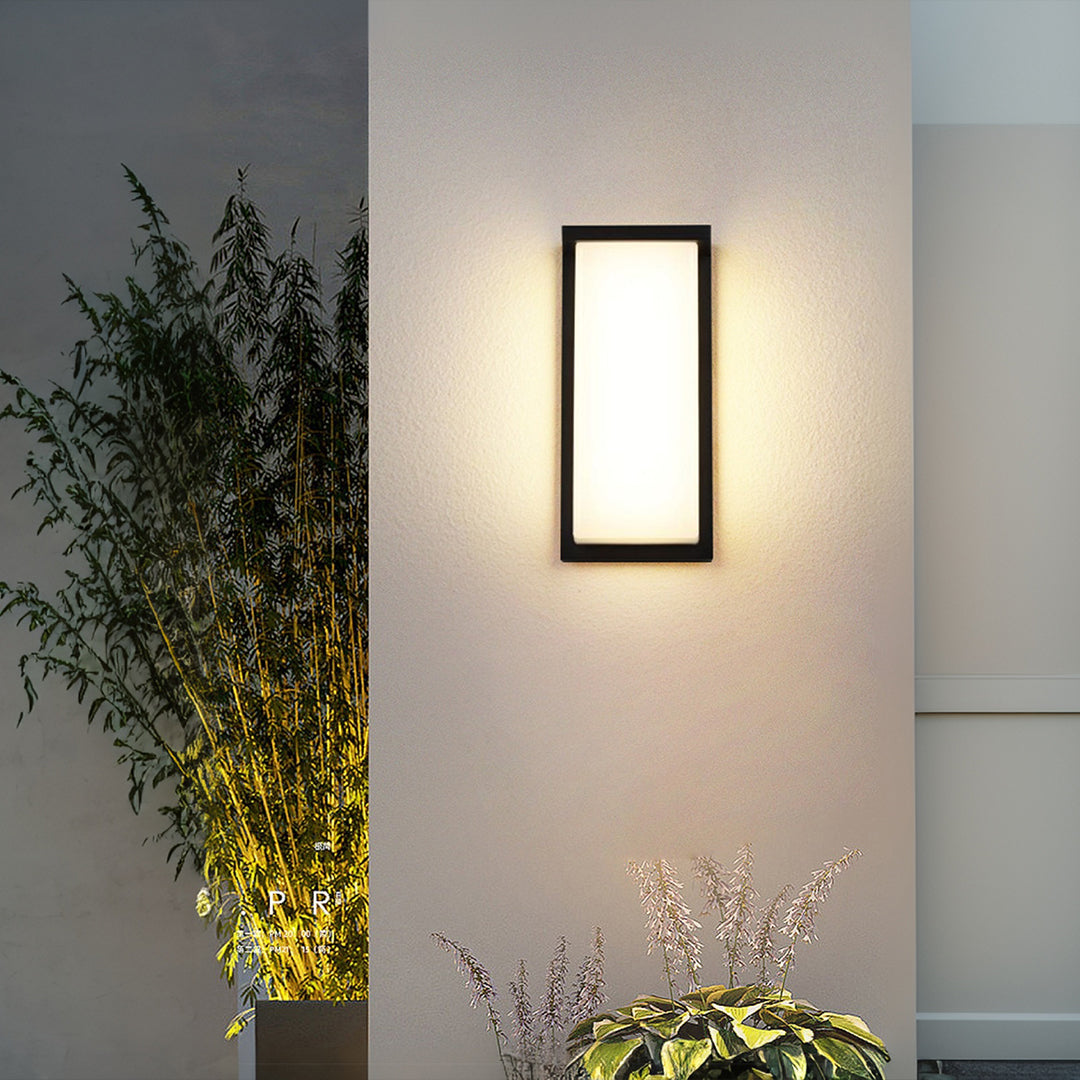 Modern wall light fixture casting soft illumination on architectural exterior with landscaping