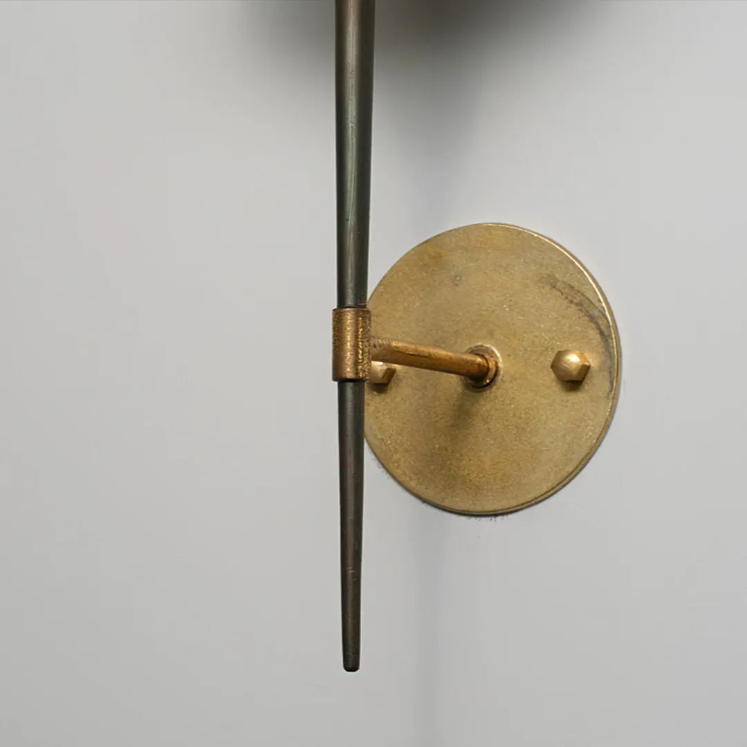 Modern wall light fixture close-up showing the brass round backplate and slim metal arm.