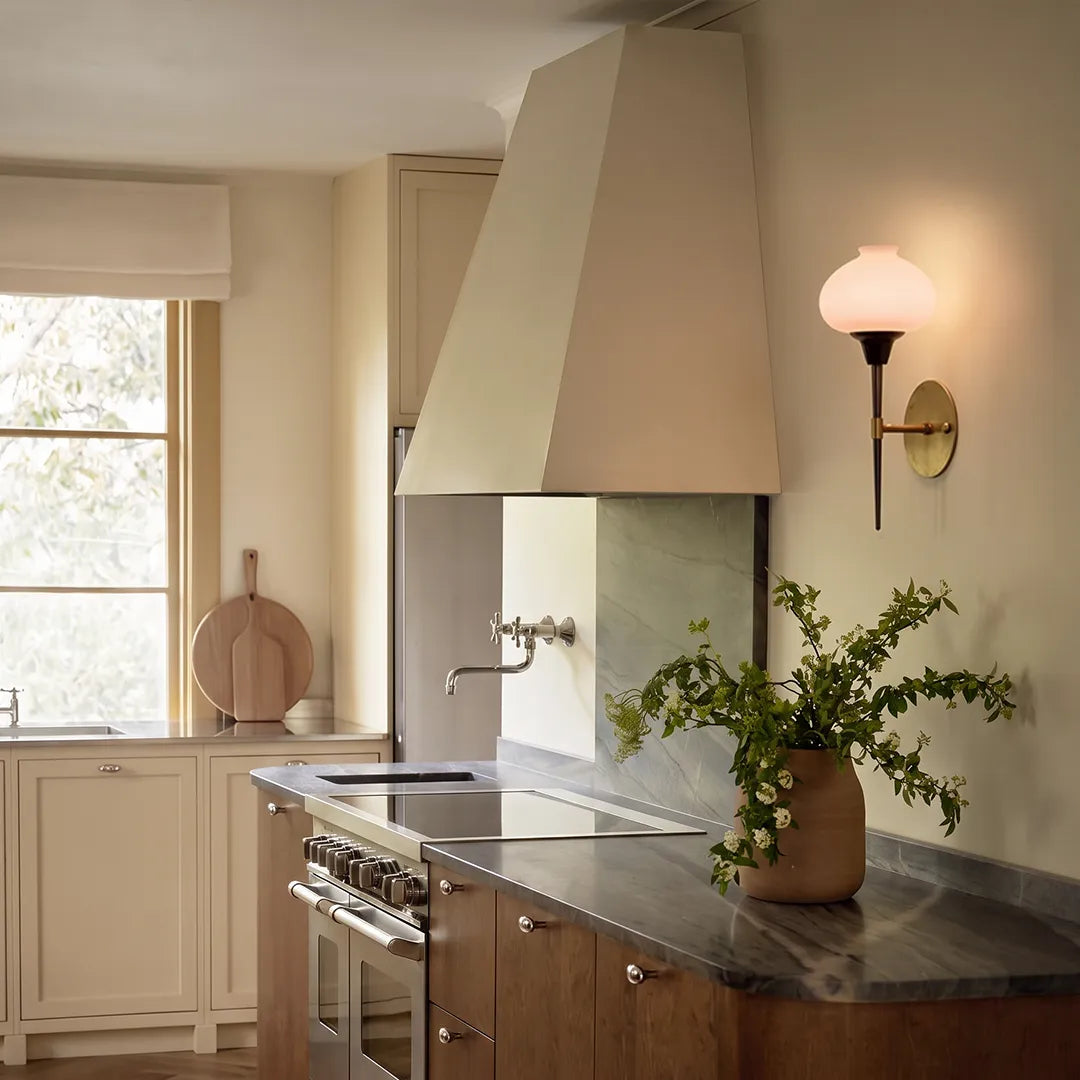 Modern wall light fixture installed in a kitchen beside a range hood with soft warm lighting.