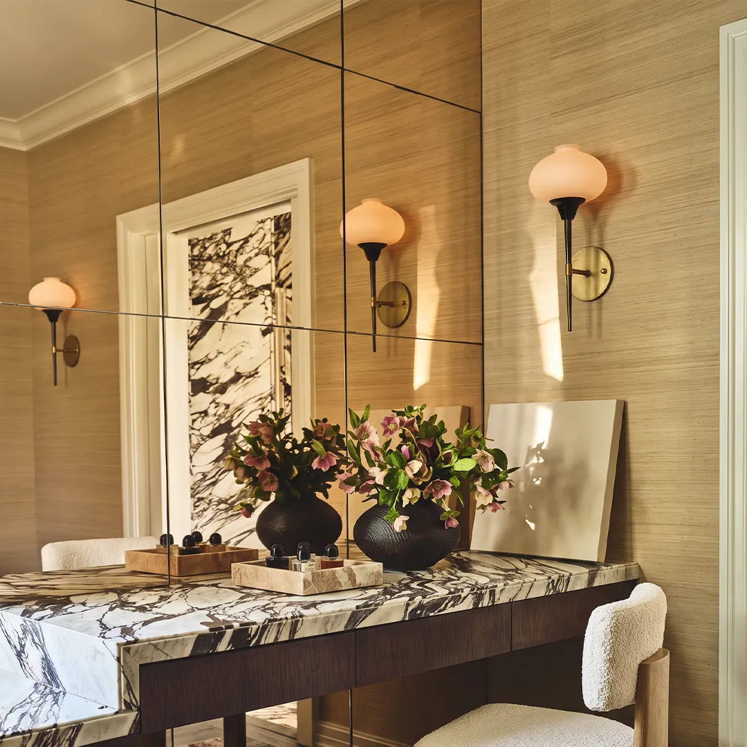 Modern wall light fixture pair reflected in a bathroom mirror above a marble vanity.