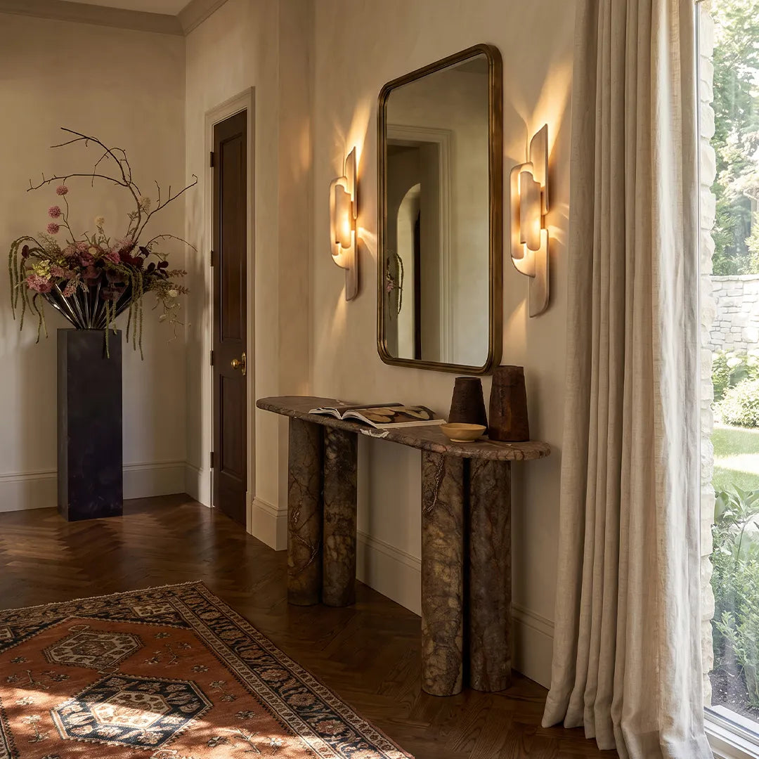 Modern wall light fixtures flanking a hallway mirror above a narrow console table.