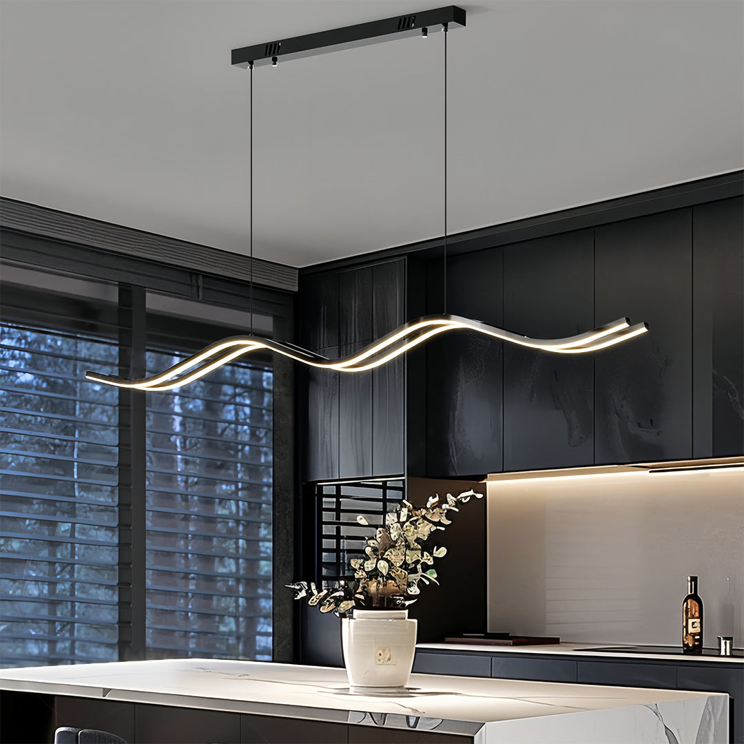 Modern black kitchen island pendant light with a wavy, linear LED design, hanging over a white marble countertop.