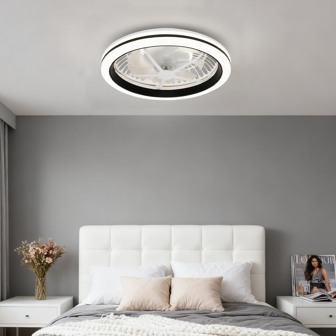 Modern circular white flush mount ceiling fan with light illuminating a bedroom with soft grey walls and a white tufted headboard. 
