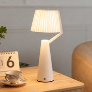 Modern white Nordic table lamp featuring a pleated fabric shade and angular design on a light wood side table. 