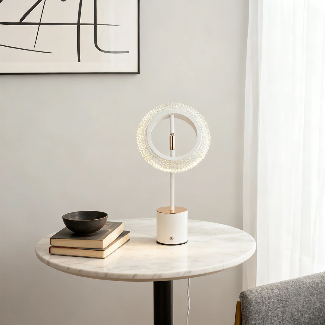 Modern white and gold ring table lamp with crystal embellishments on a marble side table in a bright room.