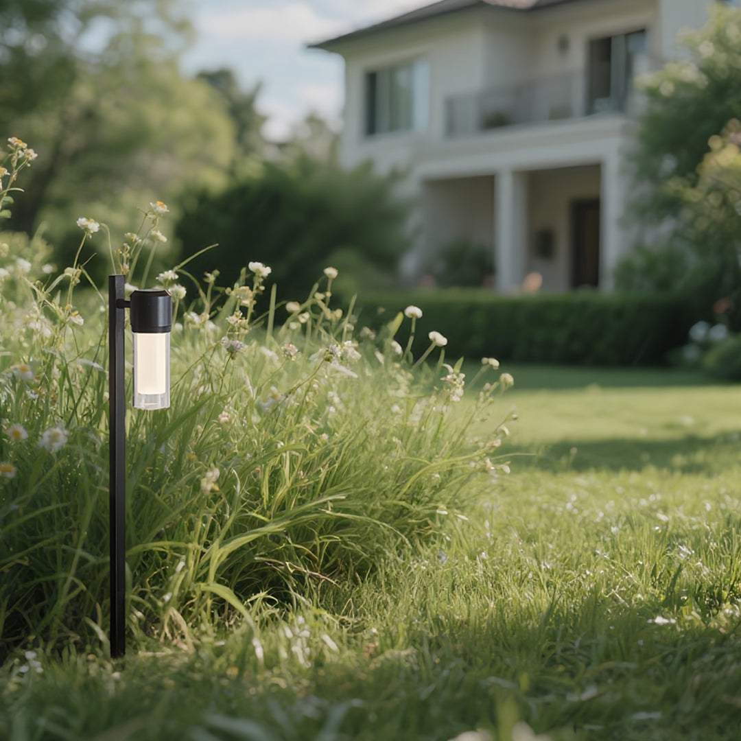 Contemporary path light placed in a grassy yard near a modern home, glowing softly at twilight.