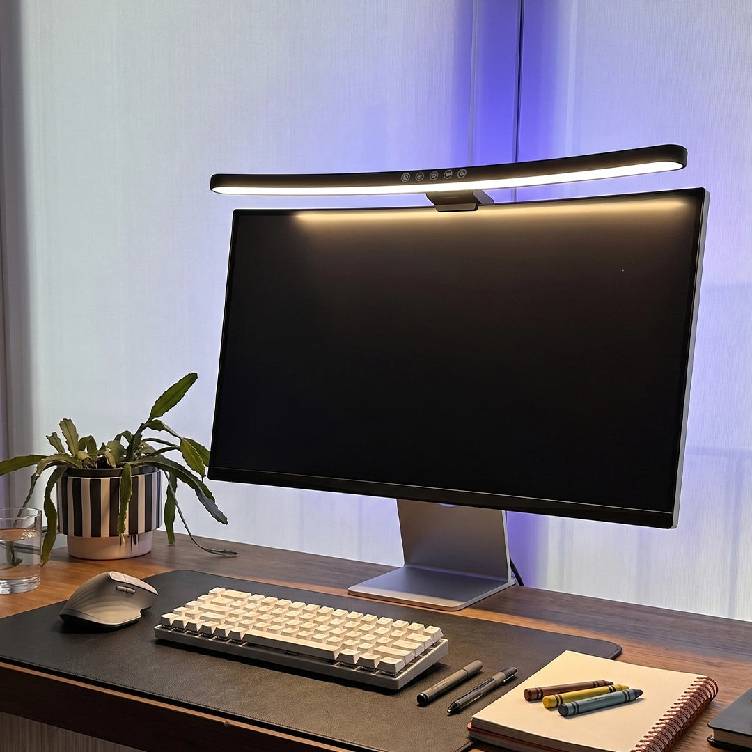 Monitor LED light bar illuminating a desktop workspace with a keyboard, plants, and warm ambient backlighting.