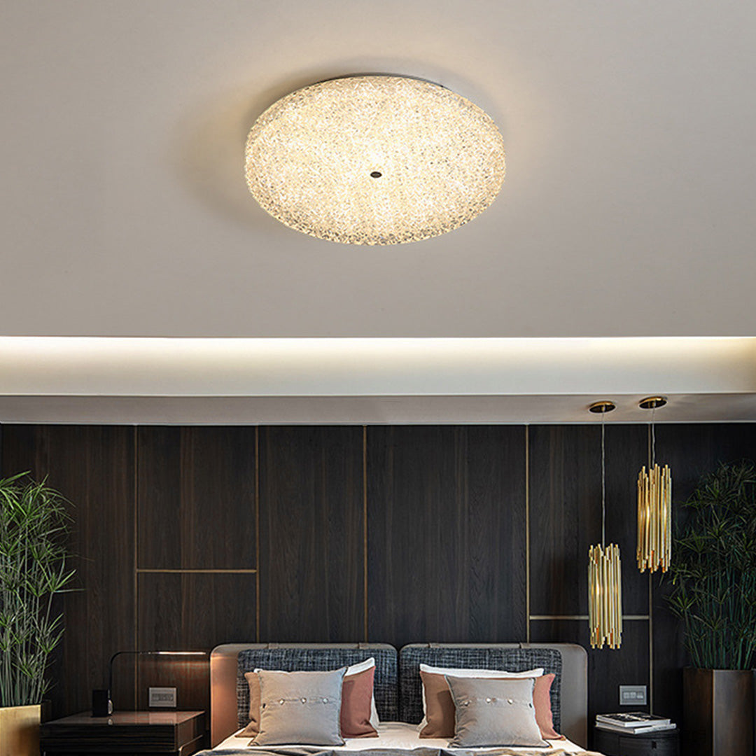 Luxurious flush mount crystal ceiling light shining above a bed in a moody wood paneled room.