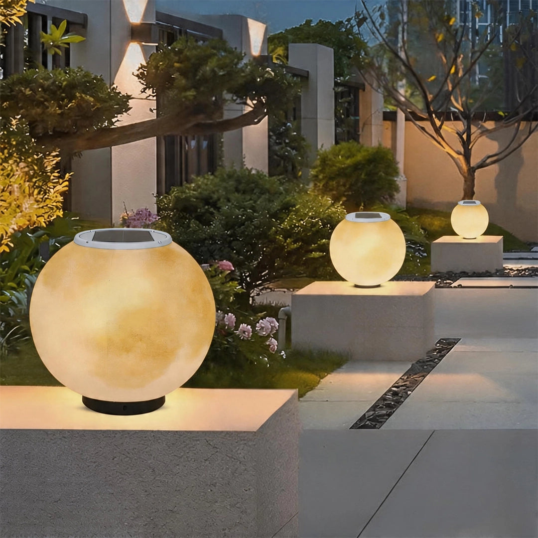Moon pillar light displayed on a concrete pedestal in a contemporary garden walkway with warm ambient lighting.