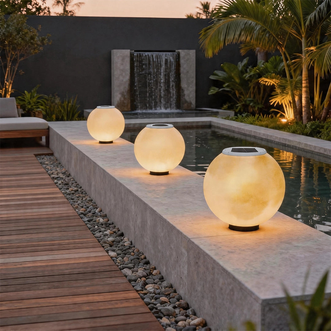 Moon pillar lights arranged along a modern poolside wall, casting a soft warm glow across the outdoor landscape.