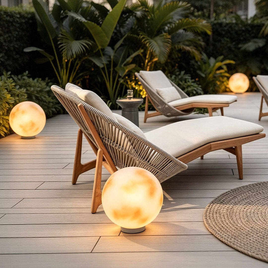 Moon-shaped stone light illuminating a poolside deck near wicker lounge seating in a tropical outdoor setting.