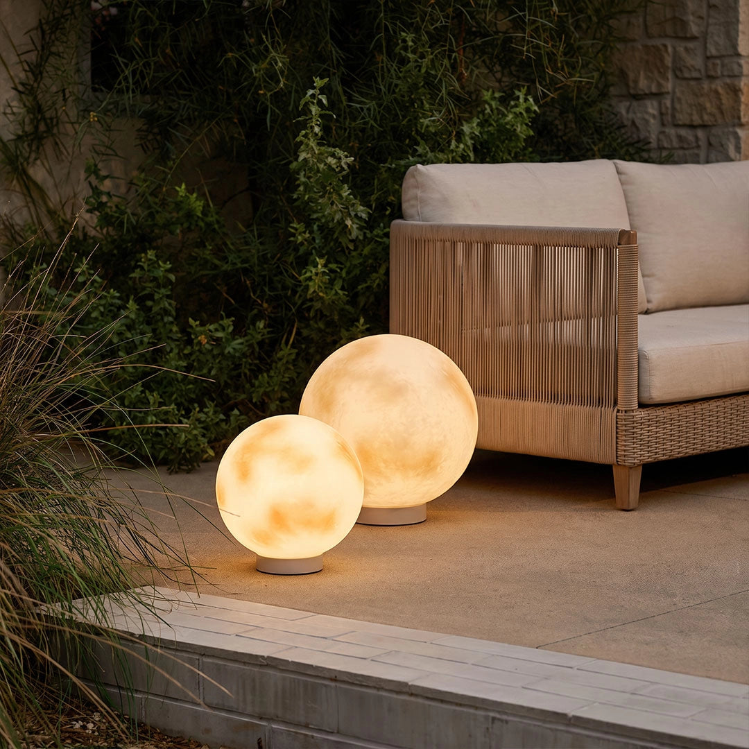 Moon-shaped stone lights placed beside an outdoor lounge chair, adding warm ambient light to a patio corner.