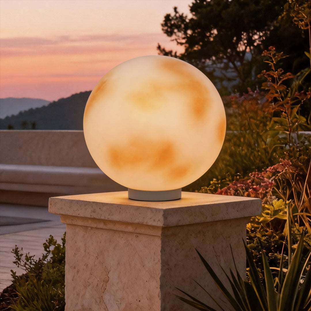 Modern moon-shaped stone pillar light glowing on a garden pedestal during a beautiful sunset ok